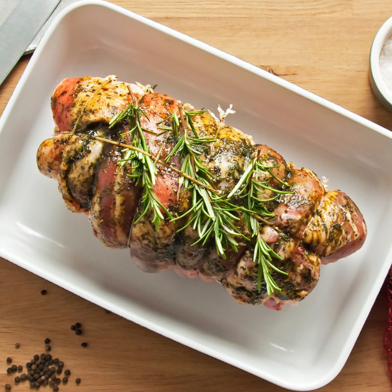 Roast lamb on a baking sheet with herbs.