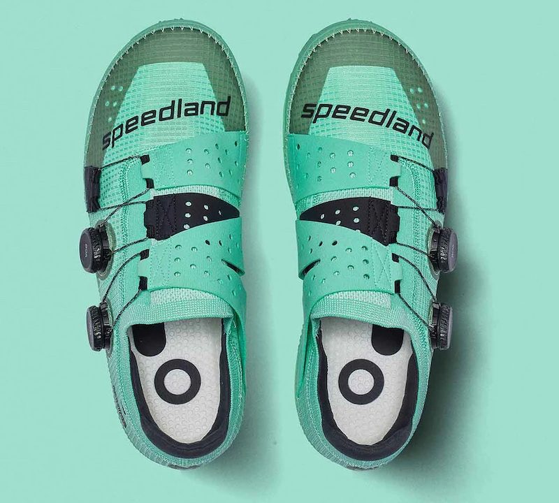 a pair of teal speedland running shoes against a teal background.