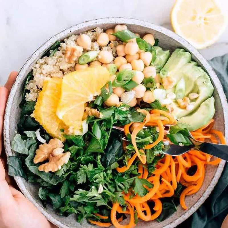 A pair of hands holding a bowl of spiralized carrot quinoa. 
