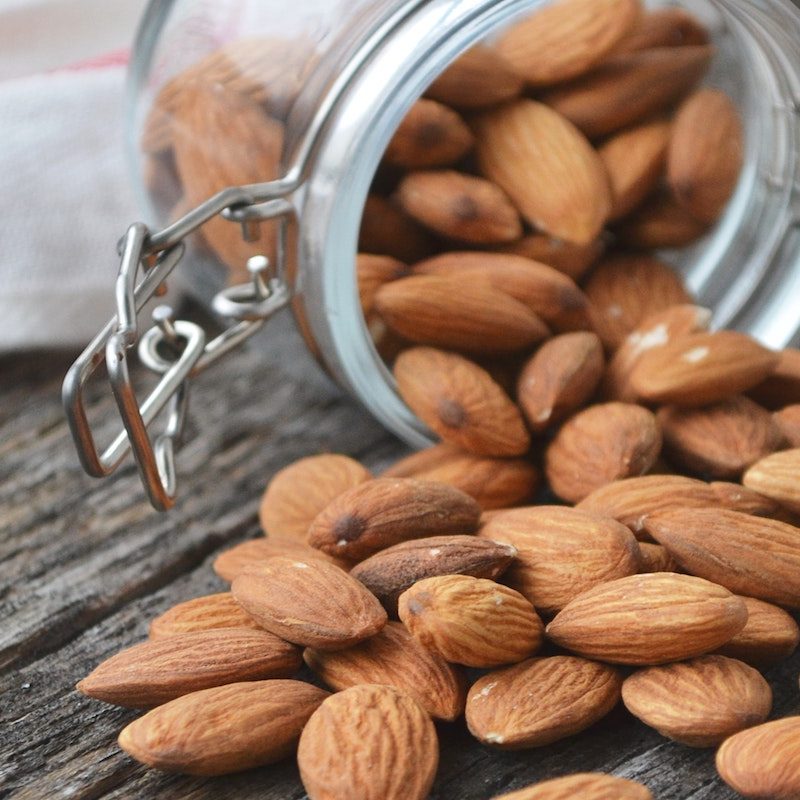 Almonds spilling out of a locking glass jar onto a wooden table.