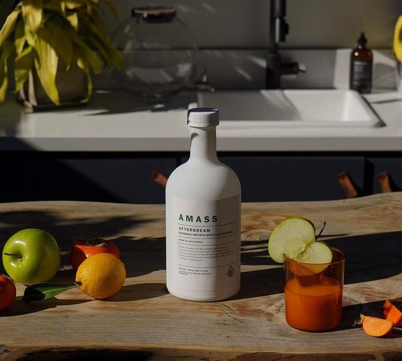 A bottle of AMASS Afterdream on a wooden kitchen counter with fruit and a candle.