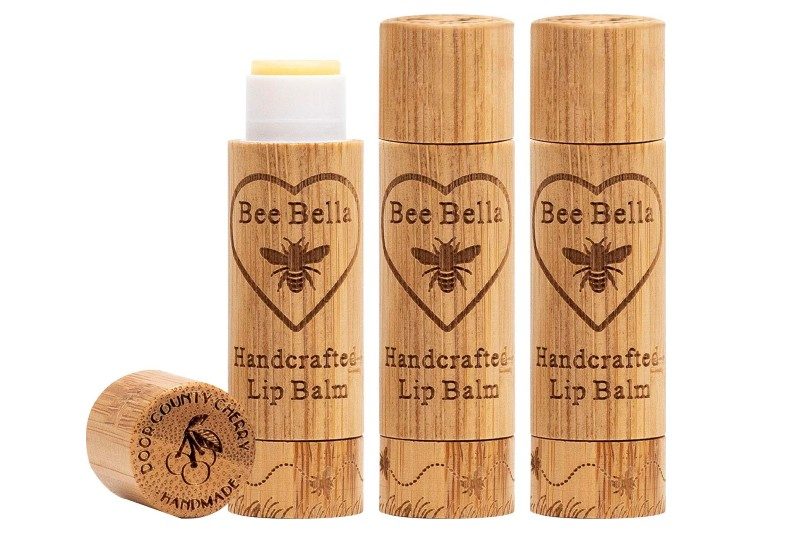 An uncapped Bee Bella lip balm beside its cap and two unopened Bee Bella lip balms.