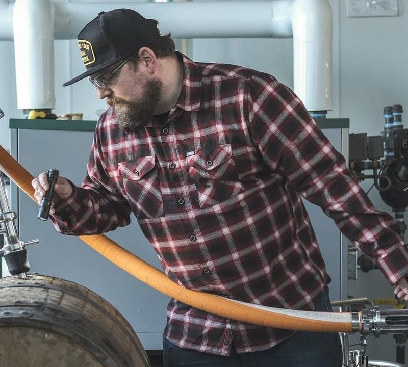 Chris Archer Ninkasi brewer inspecting a barrel of beer..