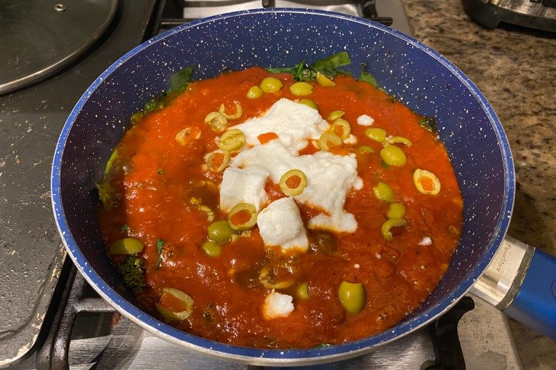 Bowl of pasta with feta cheese and green olives on top.
