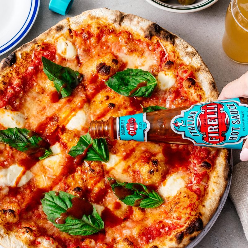 A bottle of Firelli hot sauce being poured over pizza. 