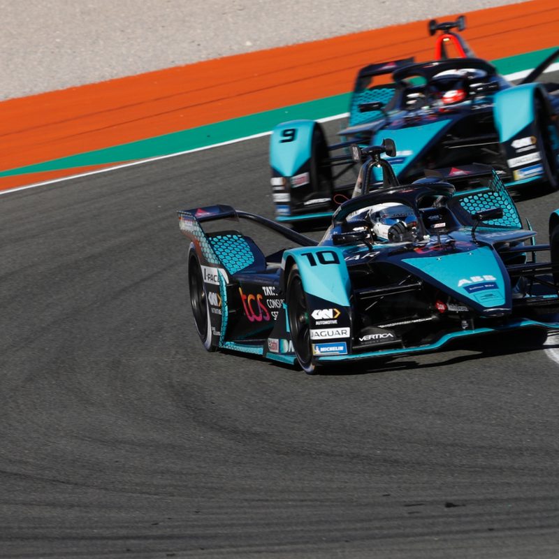 Two formula e race cars on the track.