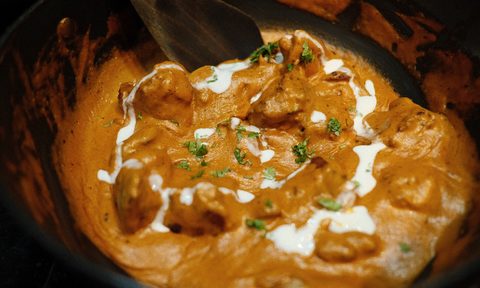 Indian butter chicken in a black pan with a spiral of cream being added.