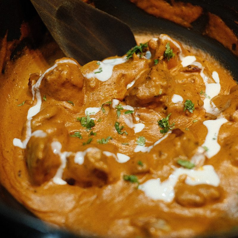 Indian butter chicken in a black pan with a spiral of cream being added.