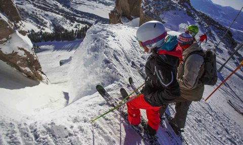 Skiiers look down couloir from the edge
