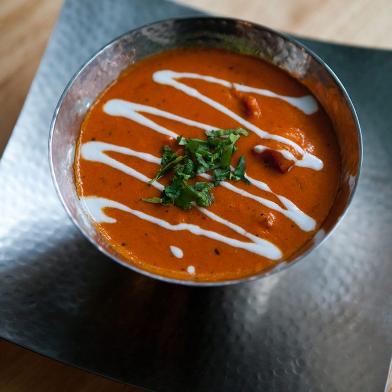 Moti Mahal Delux restaurant butter chicken topped with cream and chopped cilantro in a metal bowl on a metal plate.