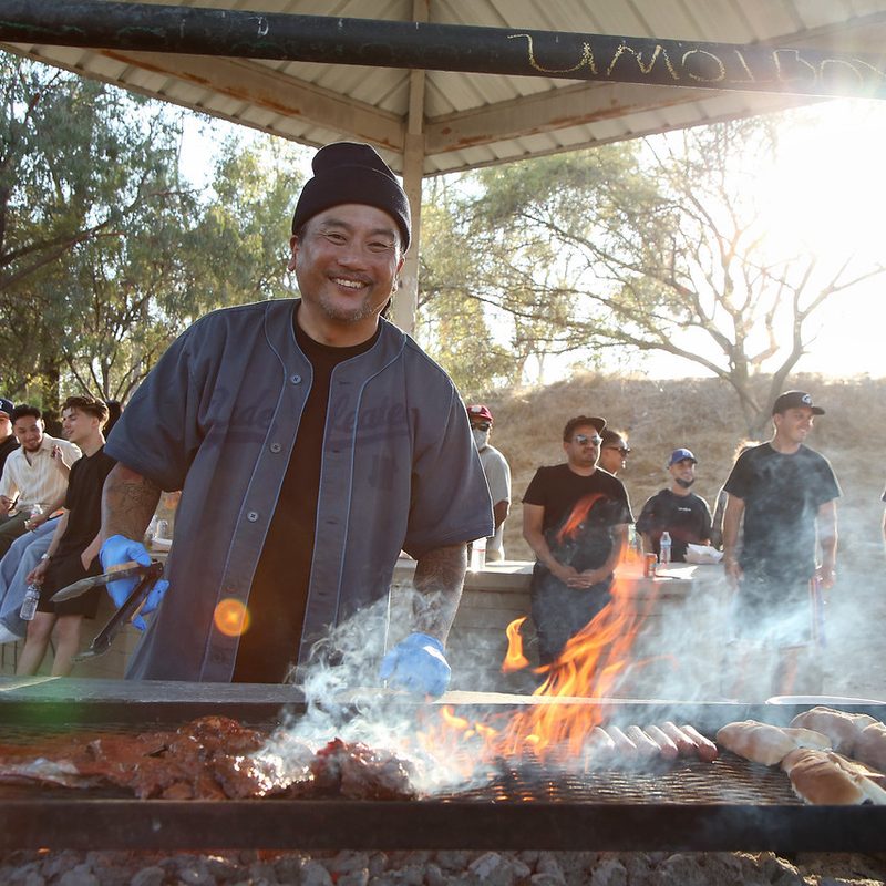 Roy Choi smiling while grilling outside for a crowd in LA's Chavez Ravine.