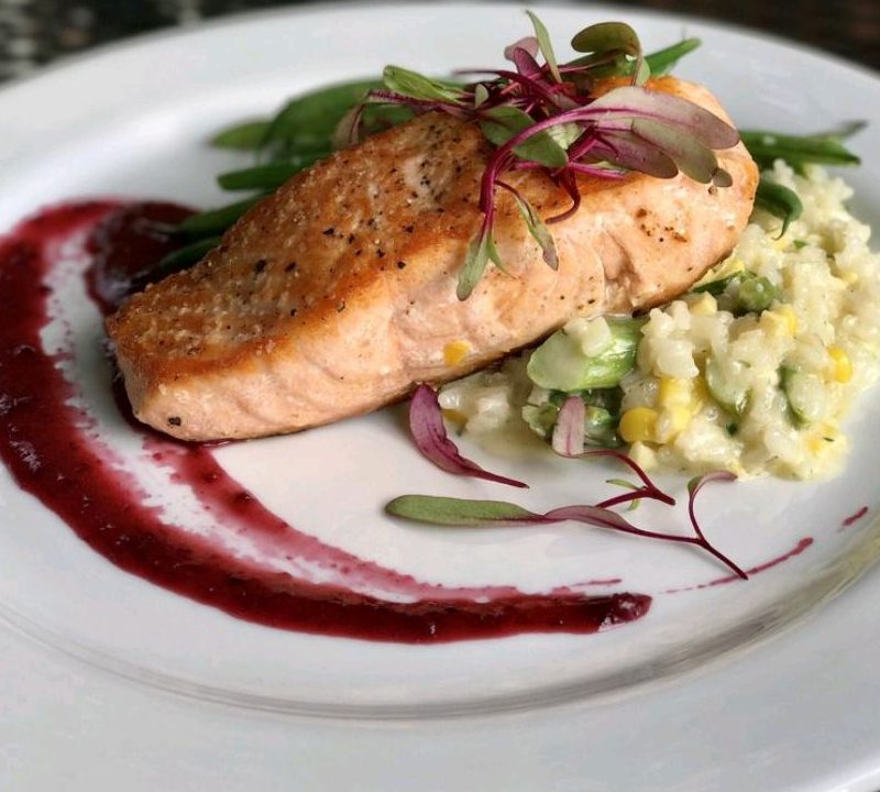 Pan fried salmon filet on a plate with side dish and garnish - Salt of the Earth Bistro
