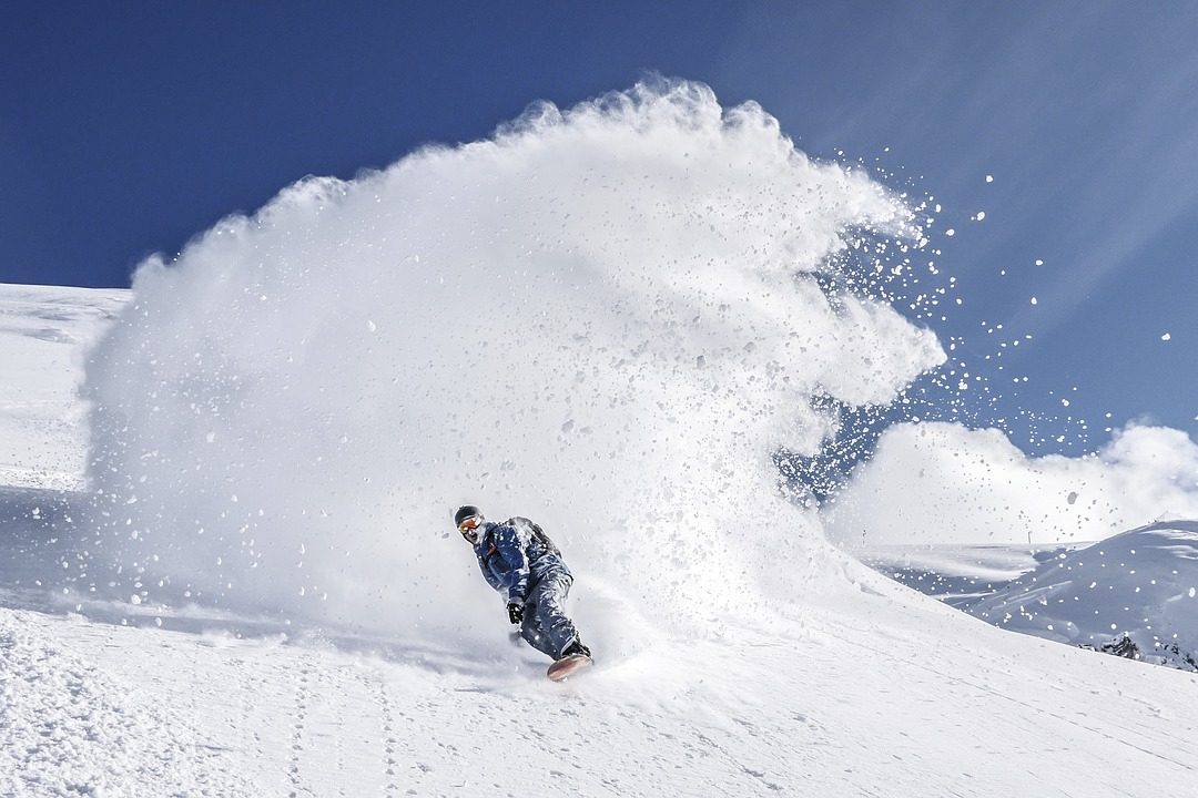 Person snowboarding down a mountain with a wake of snow behind them
