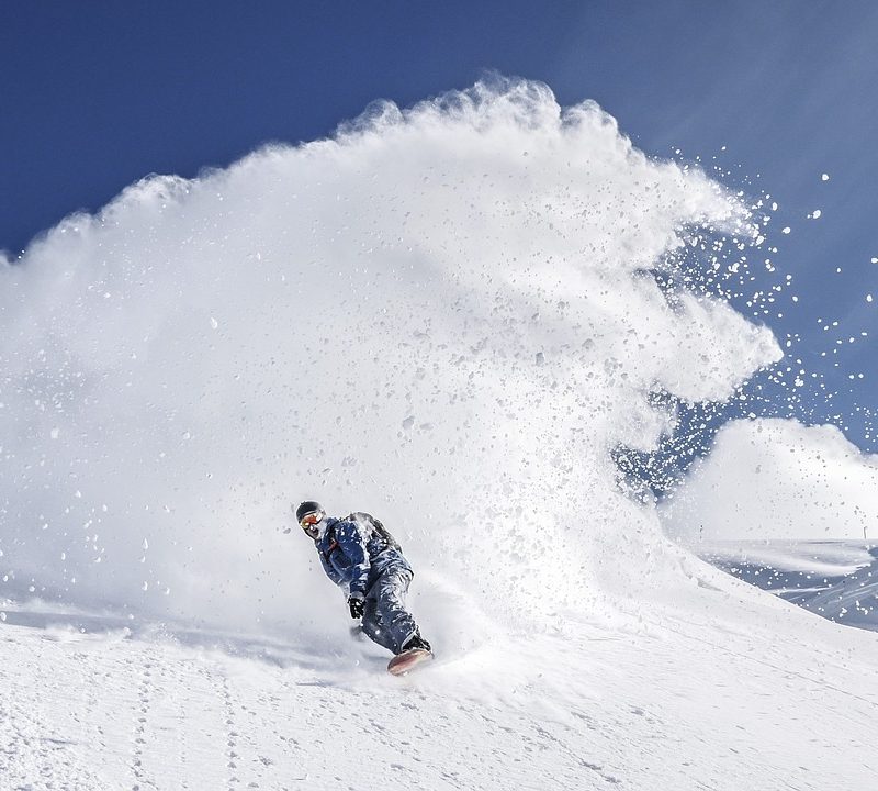 Person snowboarding down a mountain with a wake of snow behind them