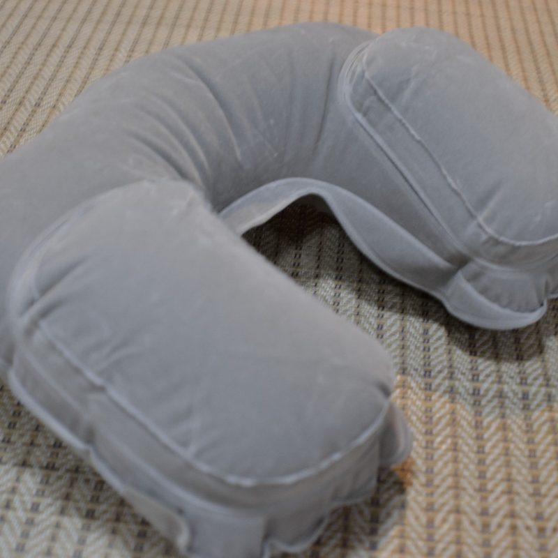 A gray memory foam travel pillow on a mat.