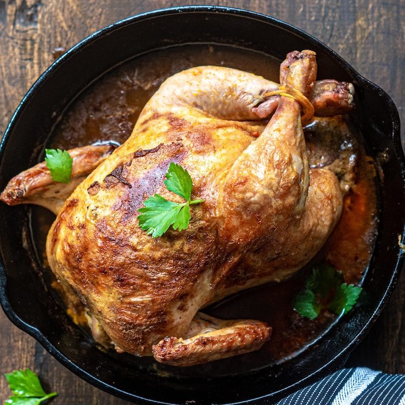 A whole roasted chicken in a cast iron pan with a parsley garnish.