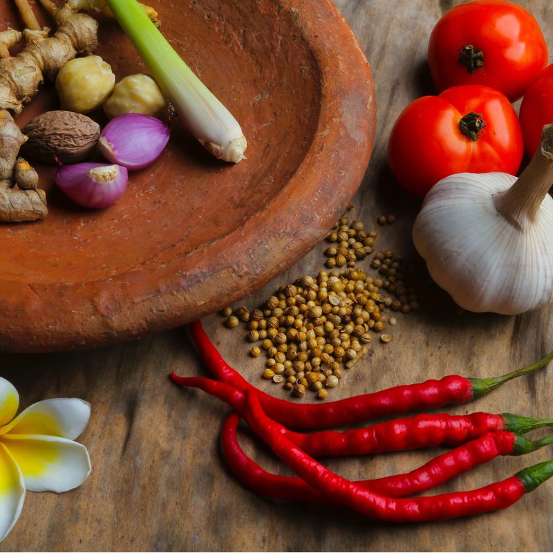 Asian ginger, lemongrass and shallots in a wooden ball next to chillies, garlic and tomatoes.