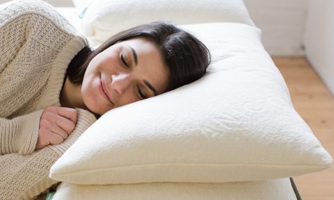 A woman rests her head on an Avocado Green pillow.