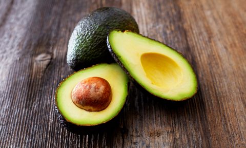 A whole avocado behind a sliced avocado on a wooden surface