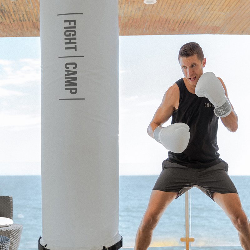 A man with boxing gloves preparing to punch a FightCamp punching bag by the sea.