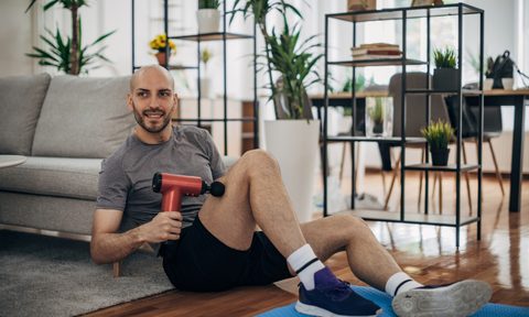 A man using a massager on his leg on a yoga mat in the living room.