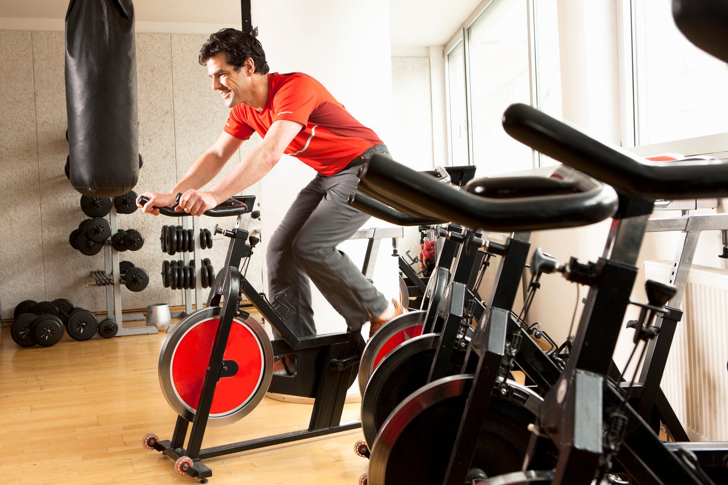 A man in red T-shirt using an exercise bike, surrounded by several exercise bikes and other fitness equipment in a gym