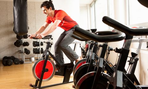 A man in red T-shirt using an exercise bike, surrounded by several exercise bikes and other fitness equipment in a gym
