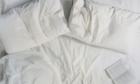 Two pillows and an opened book on a bed.
