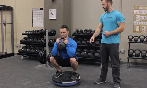 A personal trainer and his student doing a Bosu goblet squat in a gym.