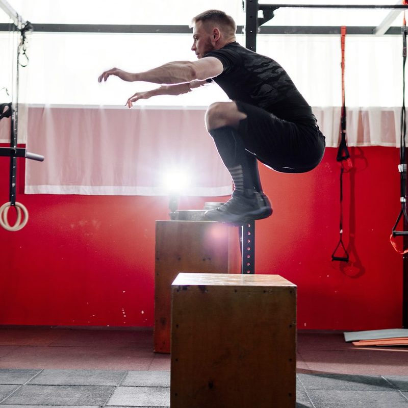 A man doing a box jump in a gym.