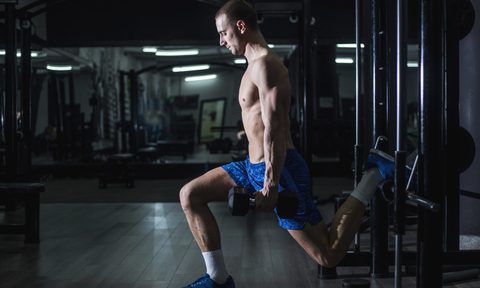 A shirtless man doing split squats using a dumbbell