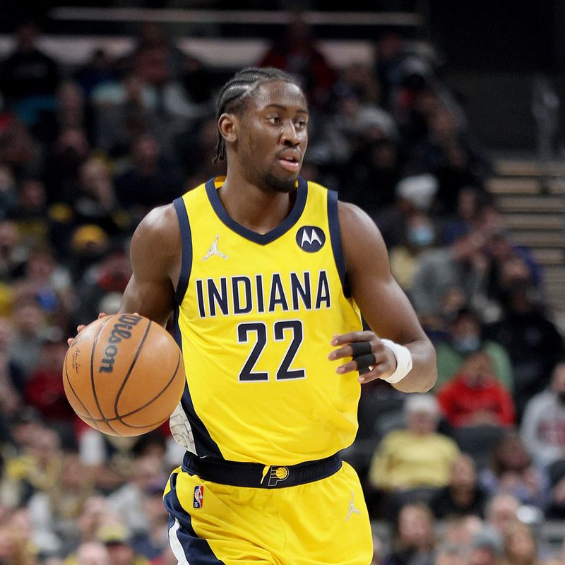 Caris LeVert dribbling a ball in the court with spectators in the background.