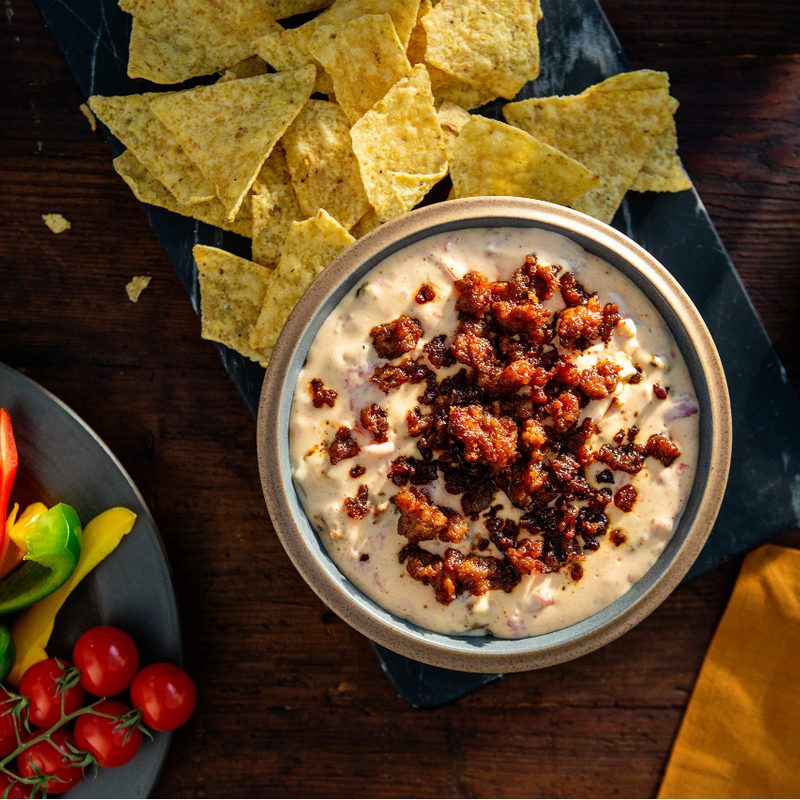 Johnsonville chorizo dip in a bowl with tortilla chips next to a plate of raw mixed veggies.