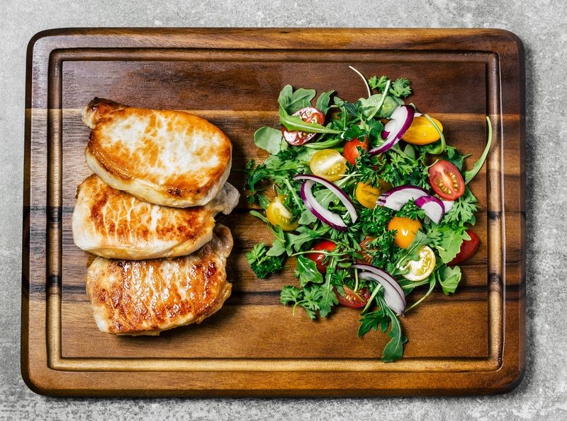 Roasted pork chops and a salad on a wooden board.