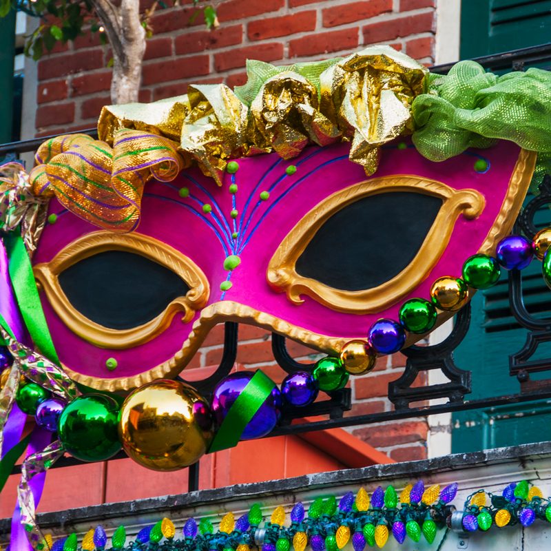 A large red-violet Mardi Gras mask on a balcony railing.