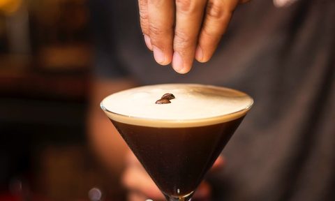 Person holding an espresso martini glass placing coffee beans as a garnish.