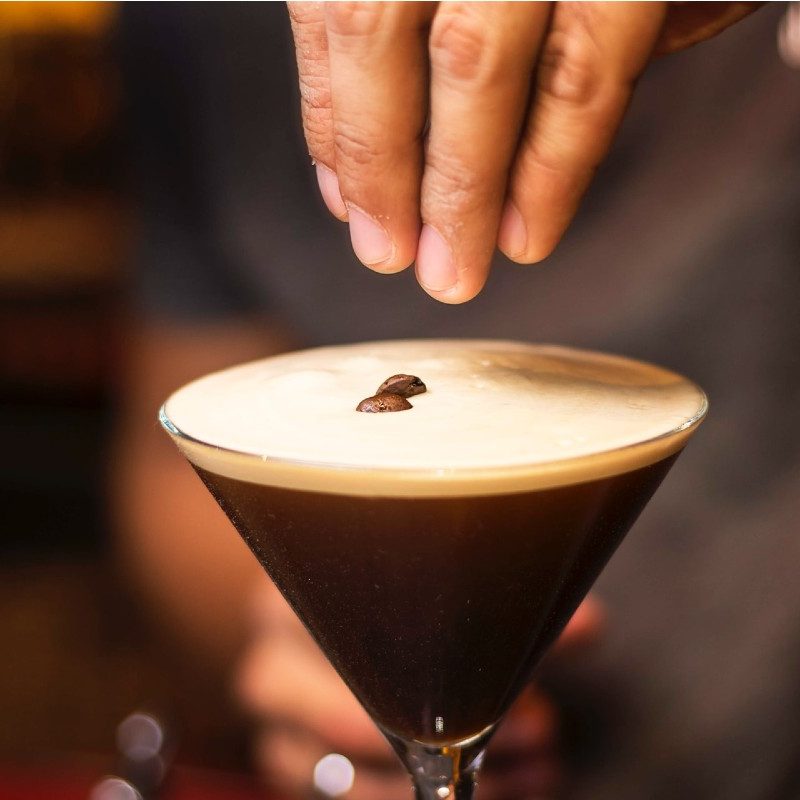 Person holding an espresso martini glass placing coffee beans as a garnish.
