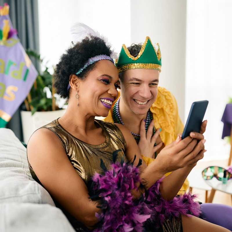 A man and a woman in Mardi Gras costumes taking a selfie in the living room.