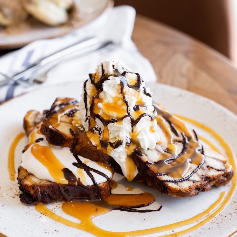 Goo Goo Cluster French toast with syrup on a white plate placed on a wooden table.