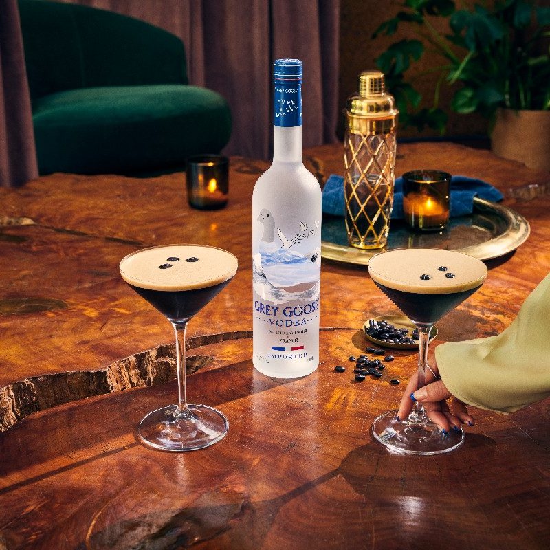 Two espresso martinis sitting next to a bottle of grey goose.
