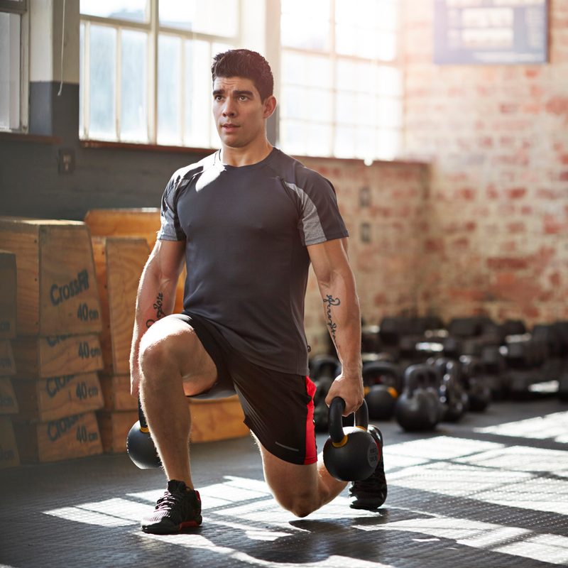 A man performing lunges with kettlebells.