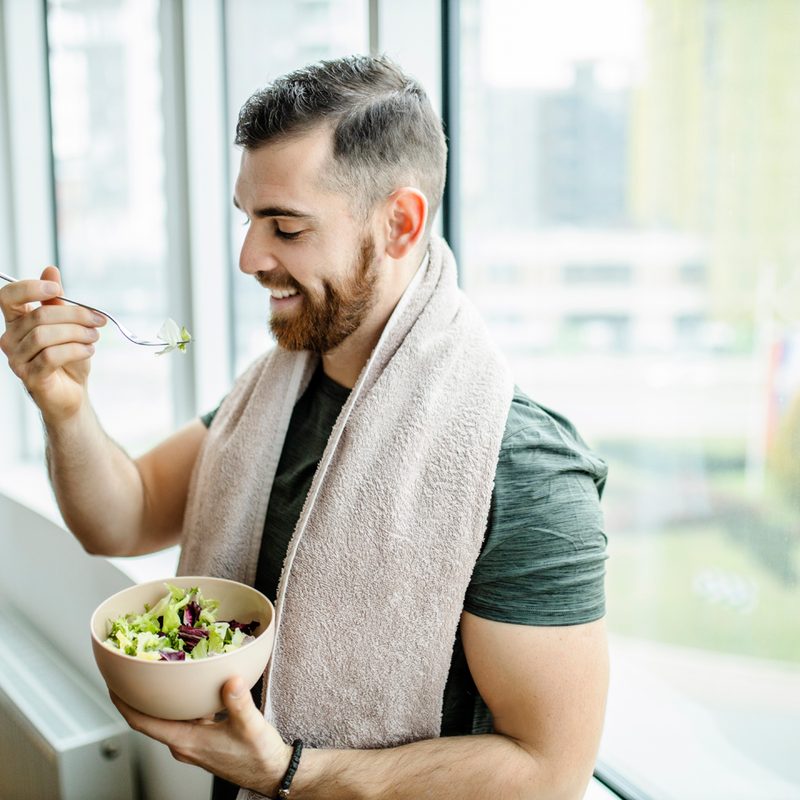 A man with a towel draped around his neck eating salad by the window.
