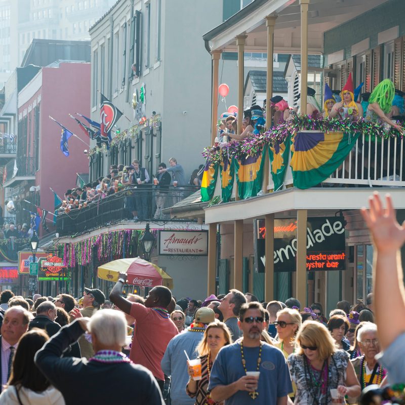 A crowd on the street and costumed individuals on a balcony during Mardi Gras.