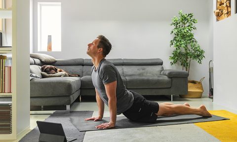 A man doing a yoga pose with a tablet in front of him in the living room.
