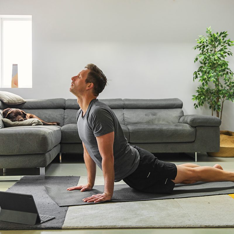 A man doing a yoga pose with a tablet in front of him in the living room.