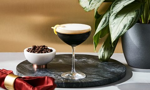 Ketel One espresso martini sitting on a tray next to coffee beans in a dish.
