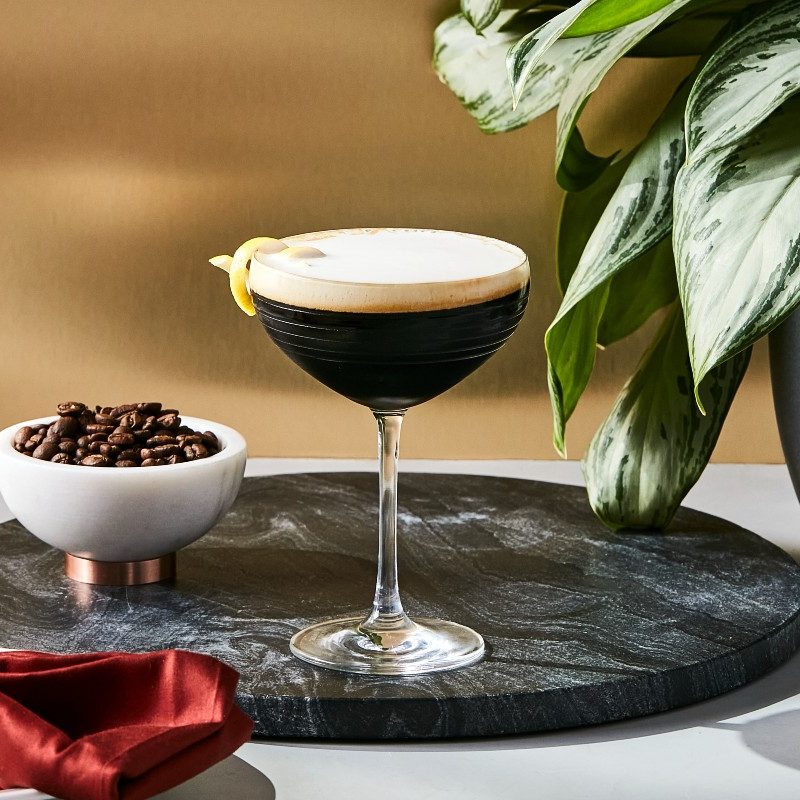 Ketel One espresso martini sitting on a tray next to coffee beans in a dish.