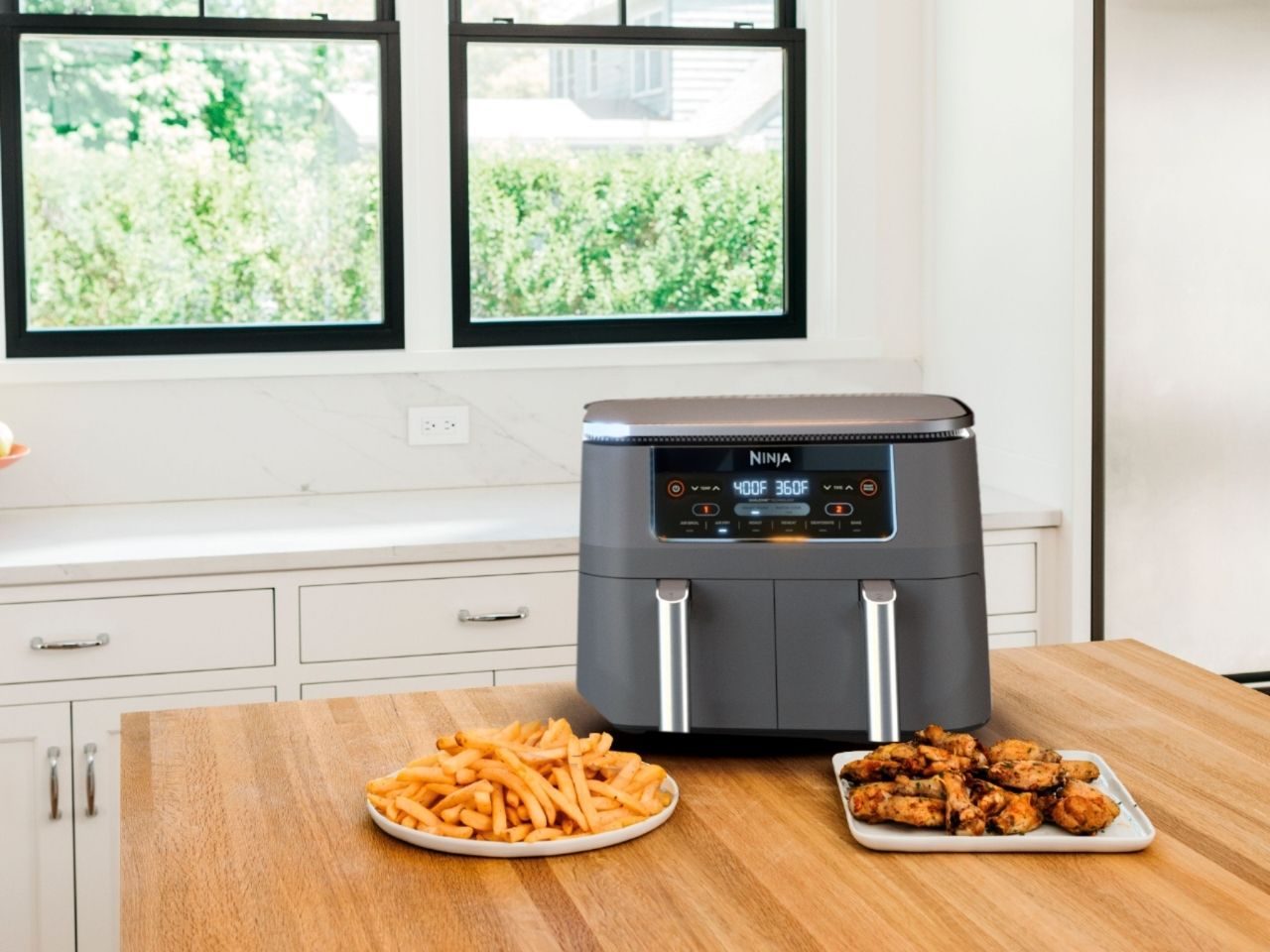 Ninja Foodi 6-in-1 air fryer with two dishes on wood table.