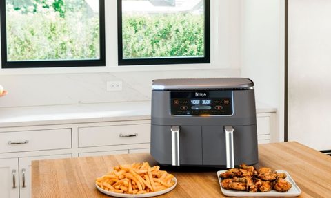 Ninja Foodi 6-in-1- air fryer with two dishes on wood table.