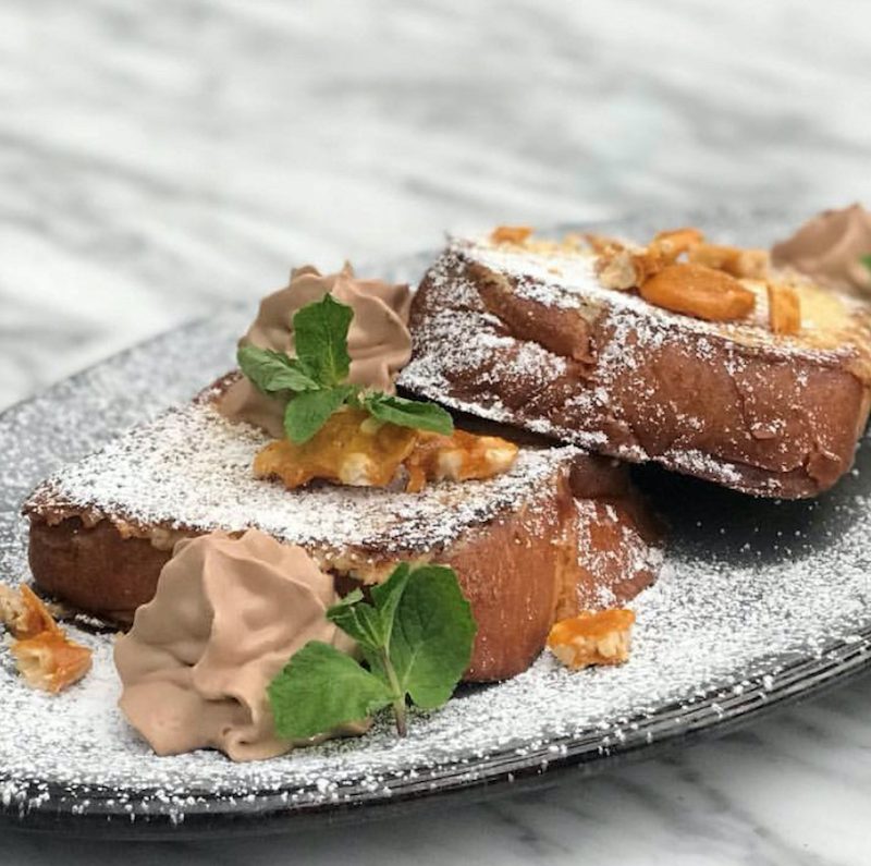 Two slices of Nutella French toast covered with powdered sugar on gray black plate.